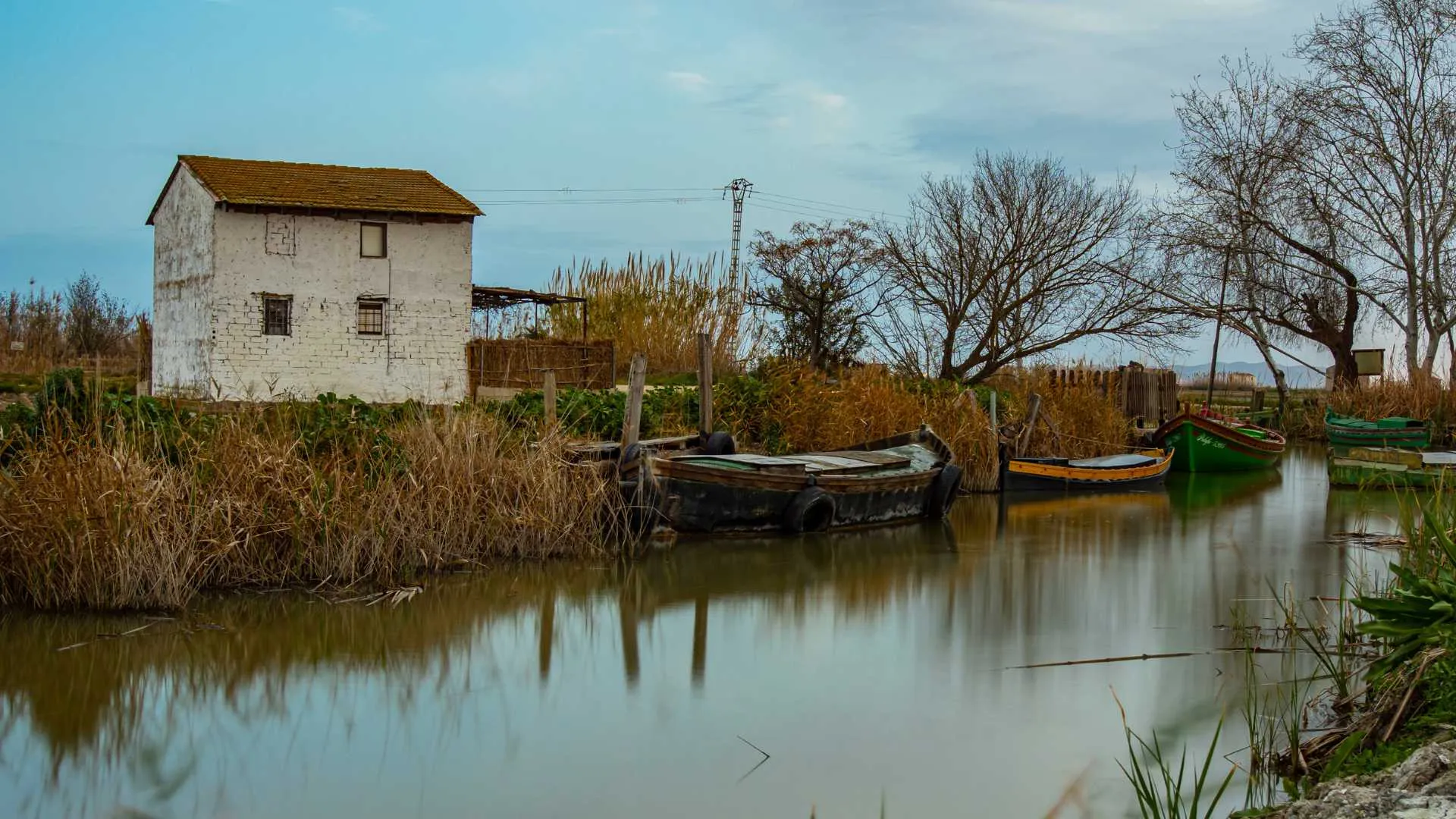 Barques de fusta amarrades a la séquia del Portet, davant d'una caseta blanca de la marjal